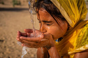Indian young girl drinking fresh water, desert village, Rajasthan, India - Slider