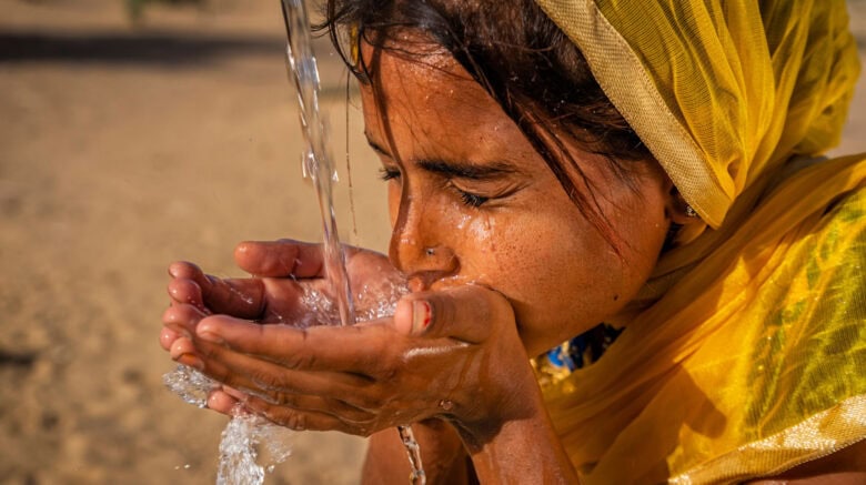 Indian young girl drinking fresh water, desert village, Rajasthan, India - Slider